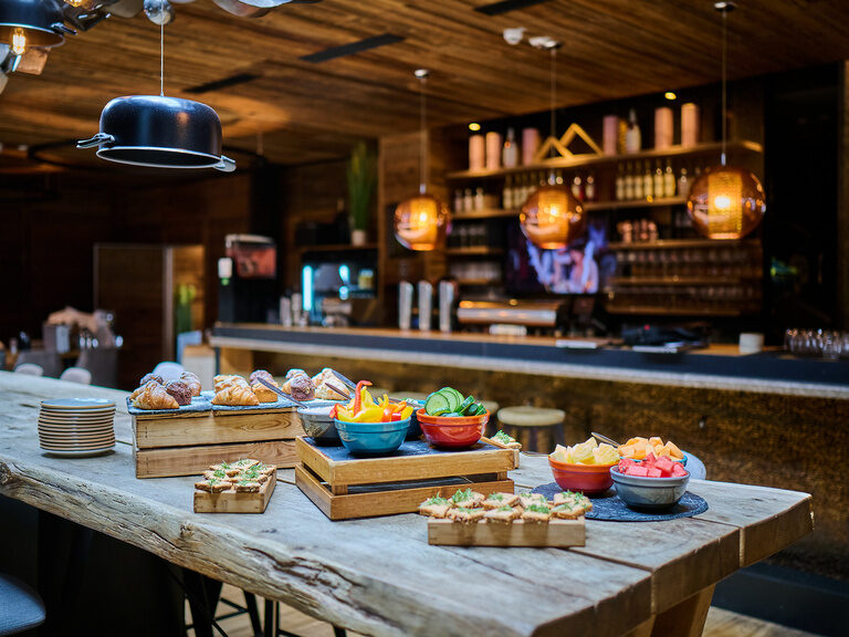 An einem rustikalen Holztisch ist am Morgen ein Frühstücksbuffet im Toni´s Gasthaus angerichtet.