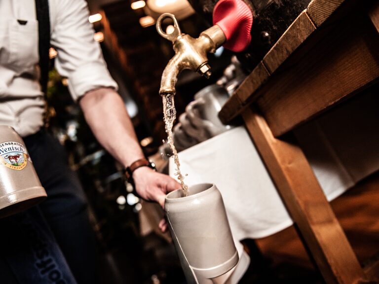 Eine Person zapft Bier aus einem Fass in einen Masskrug.