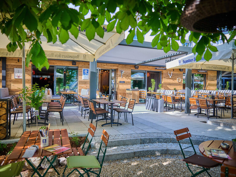 Ein Biergarten mit stilvollen Außentischen und Stühlen im Schatten von Schirmen im Toni´s Gasthaus.