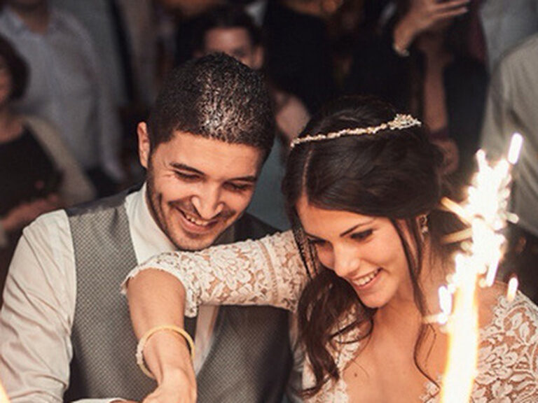 Ein Brautpaar schneidet die Hochzeitstorte, welche von Tischfeuerwerk umgeben ist, an.
