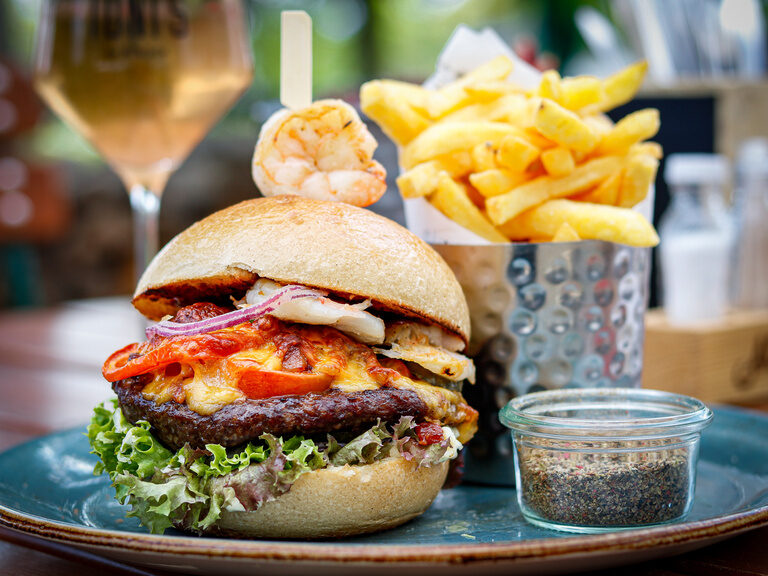 Ein saftiger Burger steht auf einer dunkelblauen Porzellanplatte und wartet darauf angebissen zu werden