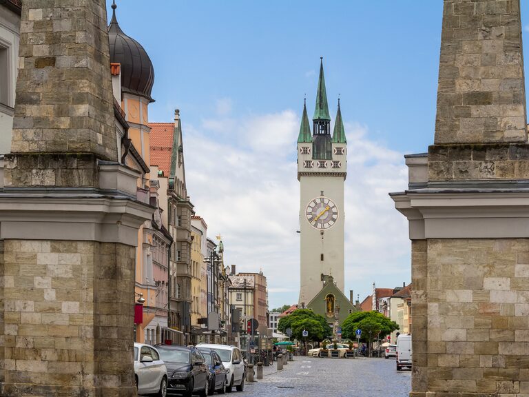 Blick durch ein Stadttor auf eine historische Altstadtstraße mit Uhrturm und bunten Häuserfassaden