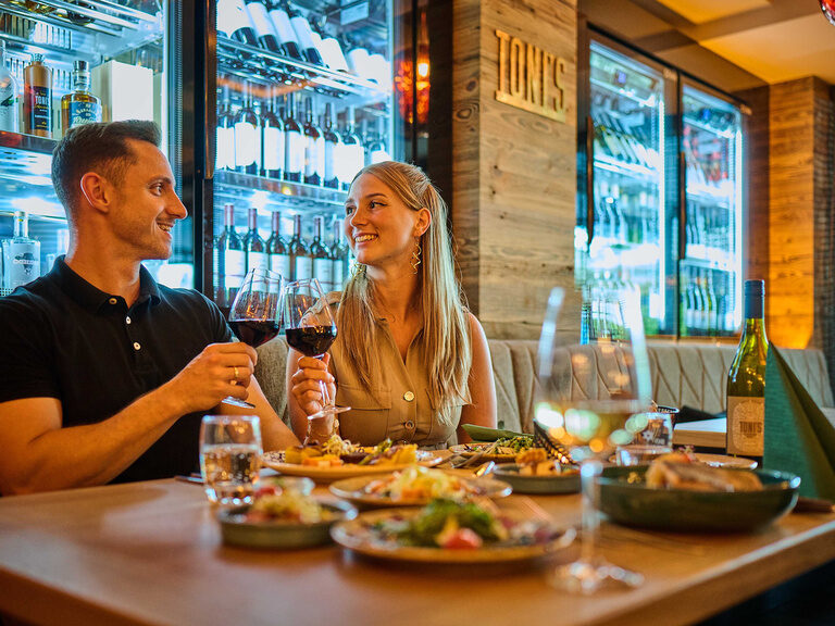 Ein Paar stößt beim Dinner for Two mit ihren Rotweingläsern an.