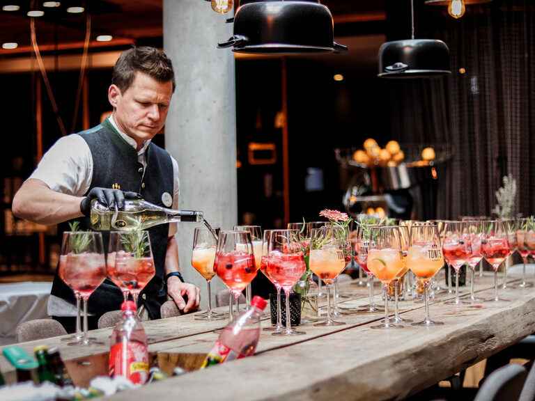 Ein Barkeeper mischt einen Cocktail und stellt ihn zu einer großen Menge an gefüllten Gläsern.