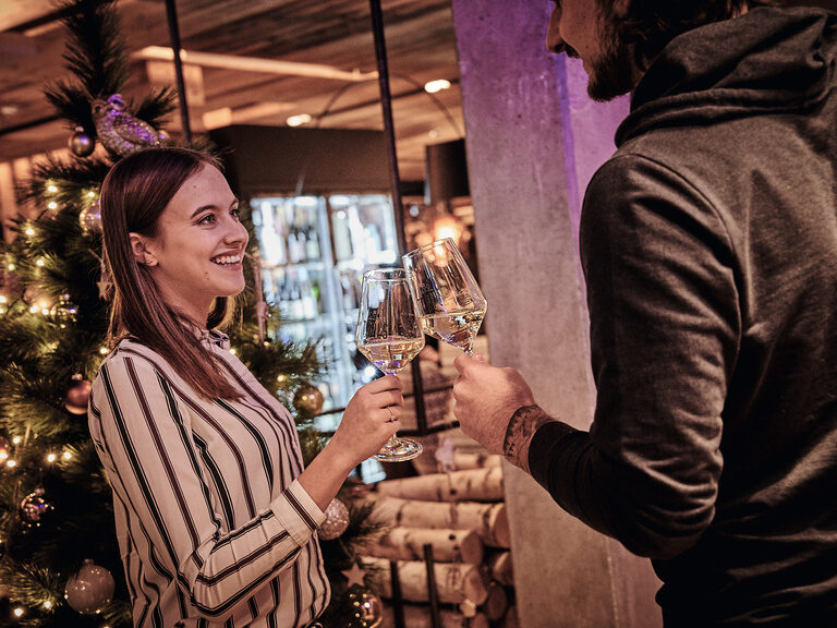 Ein Mann und eine Frau stoßen mit Weingläsern auf einer Weihnachtsfeier im Toni´s Gasthaus an.