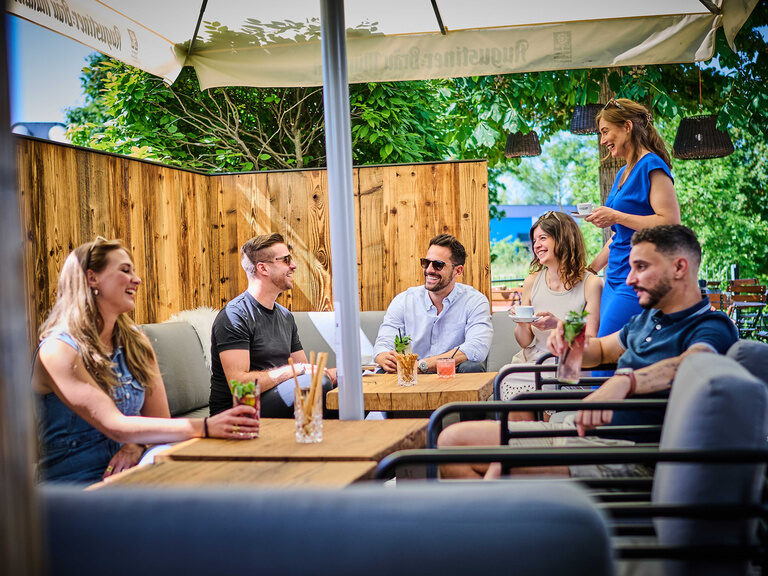 Eine gesellige Gruppe von Personen sitzt an einem Outdoor-Tisch im Genusshotel Wenisch.
