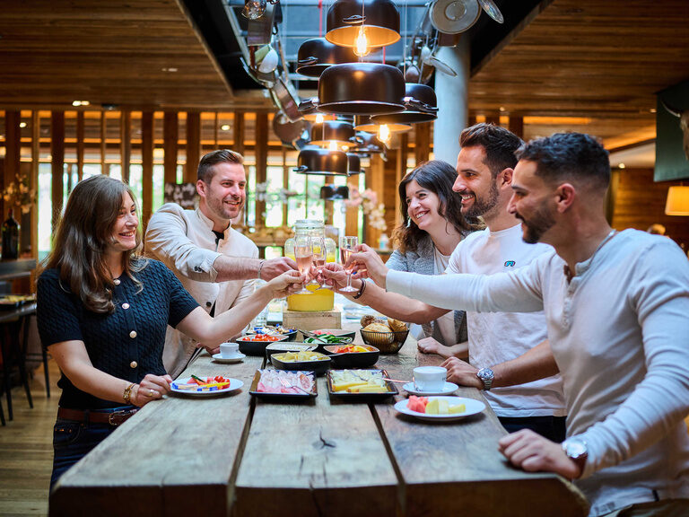 Eine Gruppe von Menschen sitzt fröhlich an einem Holztisch im Restaurant beim Brunch..