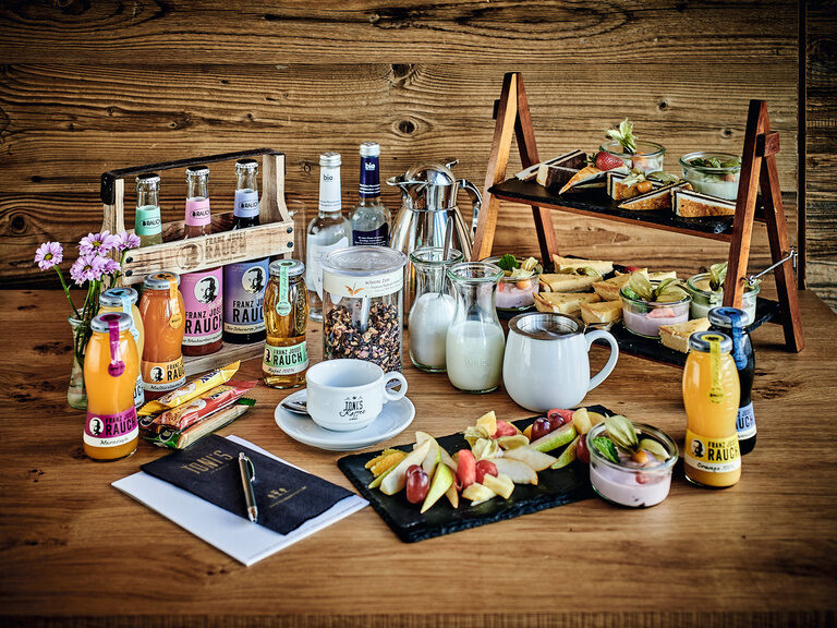 Ein reich gedeckter Holztisch mit Speisen und Getränken beim Frühstücksbuffet.