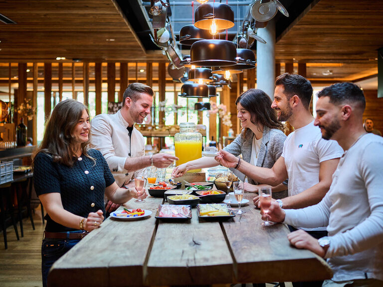 Eine Gruppe von Personen unterhält sich an einem hölzernen Tisch im Restaurant.