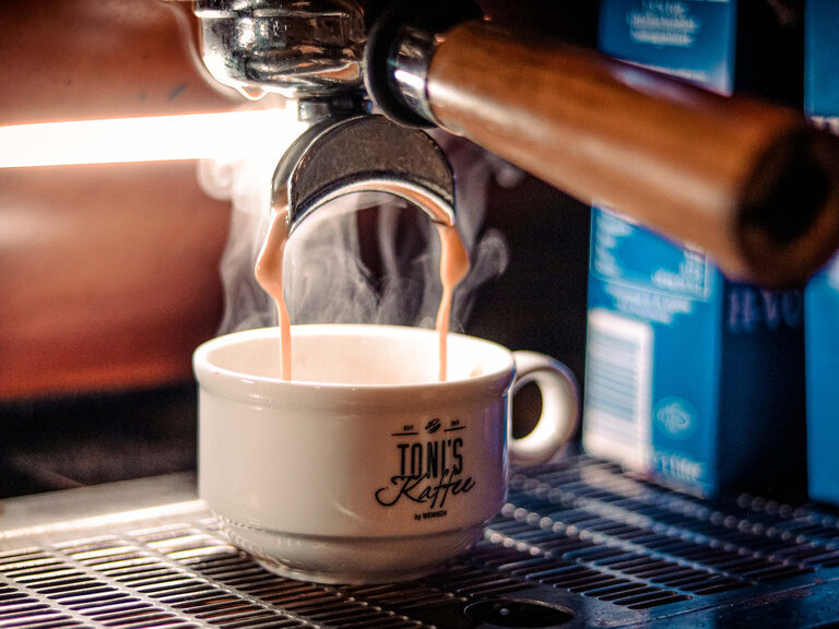 In eine Tasse fließt heißer Kaffee aus einer Kaffeemaschine.