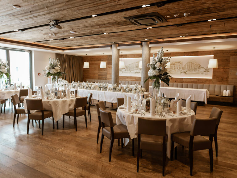 Ein großer Hochzeitssaal ist bereits für eine Hochzeit schön hergerichtet mit Blumendoeko und Gläsern.