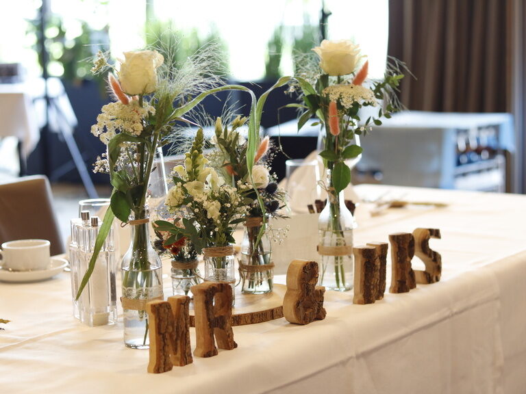 Ein eleganter Tisch mit Blumenschmuck und zwei Holzaufsteller mit der Aufschrift MR & MRS.
