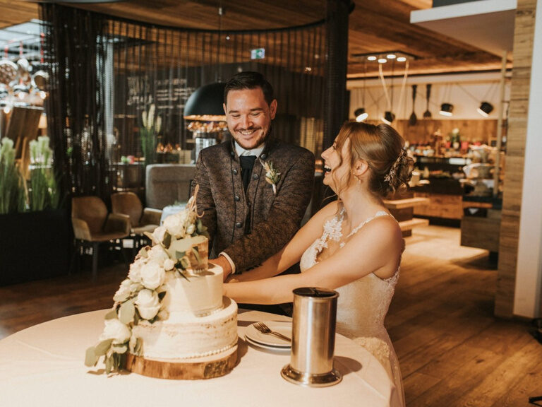Ein Brautpaar schneidet die mit Blumen verzierte Hochzeitstorte an.