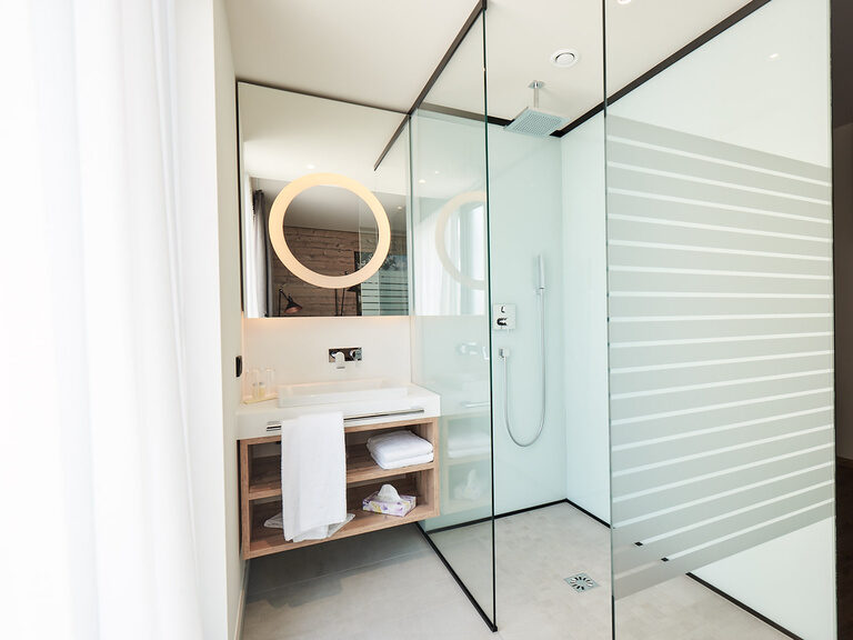 Ein stilvolles Badezimmer im Komfort Deluxe Zimmer des Genusshotels Wenisch mit einem modernen Waschbecken und Spiegel.