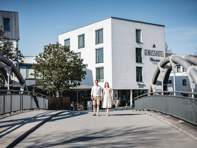 Ein Paar spaziert die Straße entlang vor dem Genusshotel Wenisch in der urbanen Umgebung.