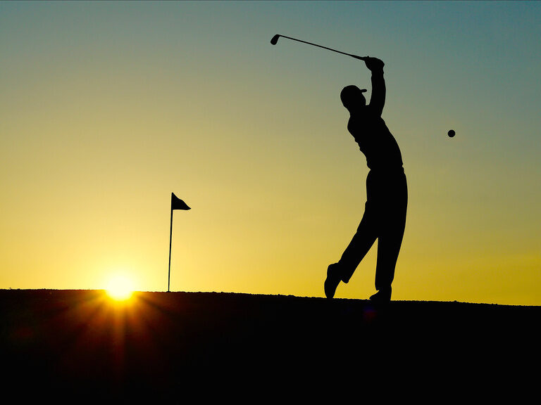 Ein Golfer schwingt seinen Schläger auf einem Golfplatz bei Sonnenuntergang.