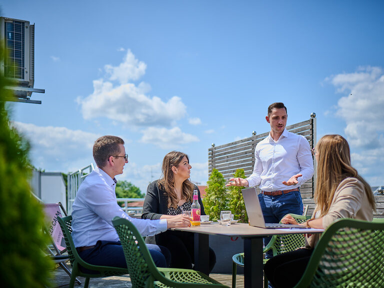 Eine Gruppe von Personen nutzt an einem schönen Tag die private 40 Quadratmeter Terrasse des Raum Max im Genusshotel Straubing.