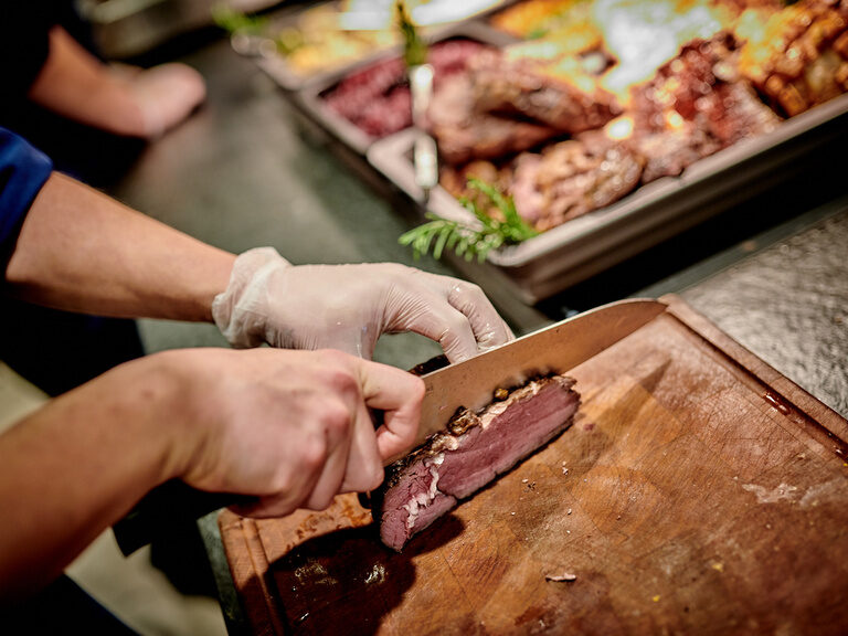 Eine Person schneidet Fleisch auf einem Schneidebrett im Toni's by Wenisch.