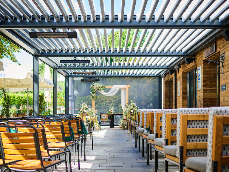 Vorbereiteter Traubereich unter moderner Pergola mit Blumen und Stuhlreihen