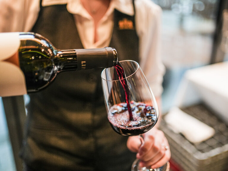 Ein Glas Rotwein wird von einer Frau eingeschenkt.